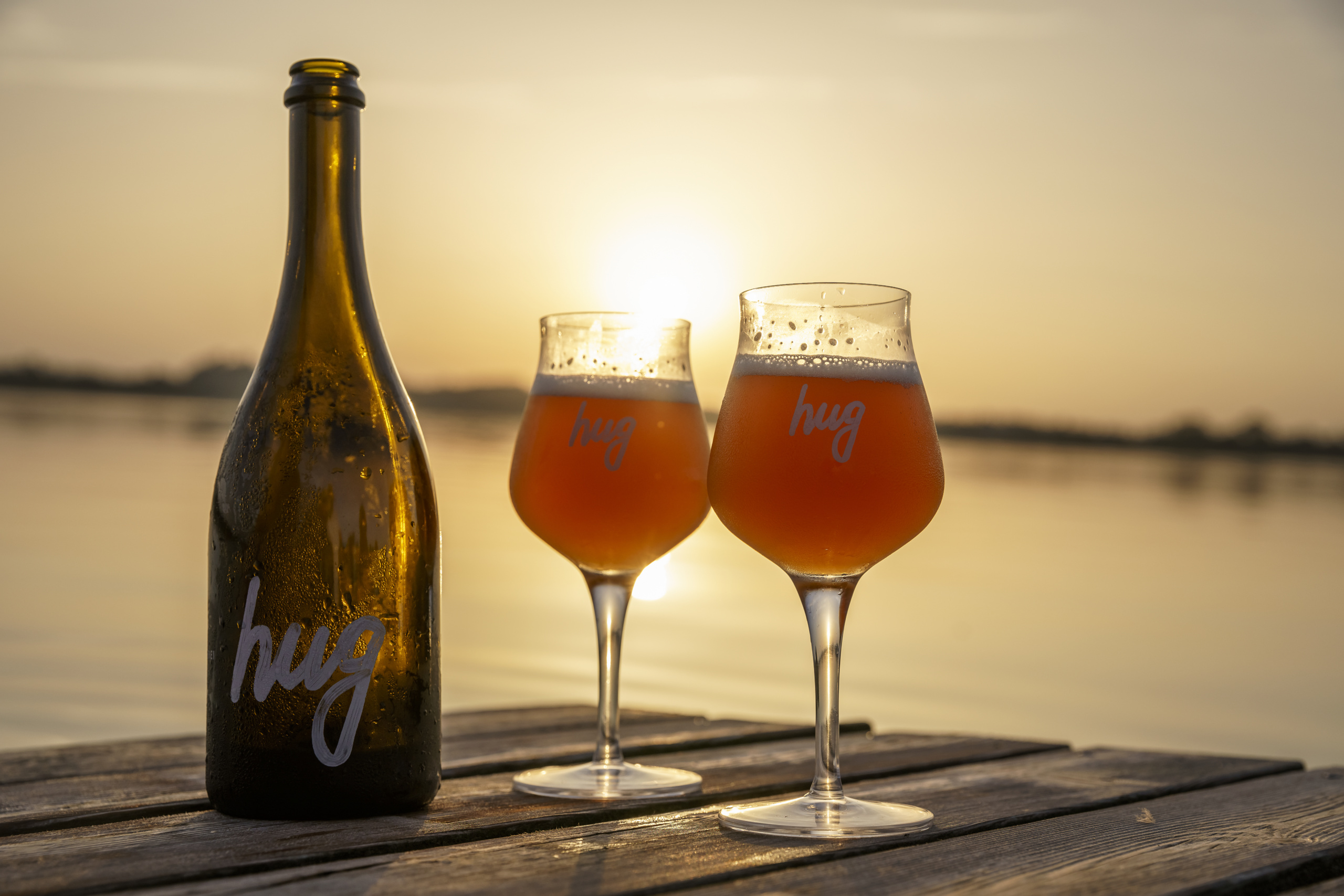 Bierflasche und Gläser auf einem Steg bei Sonnenuntergang